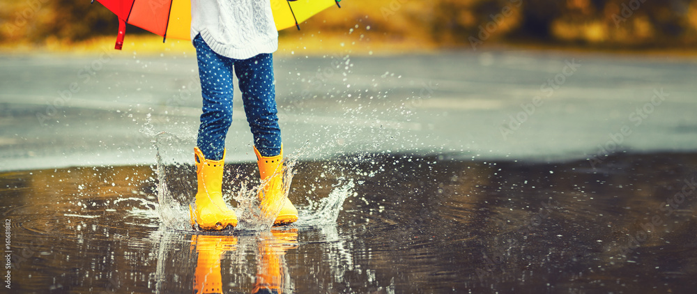 Obraz premium Feet of child in yellow rubber boots jumping over puddle in rain