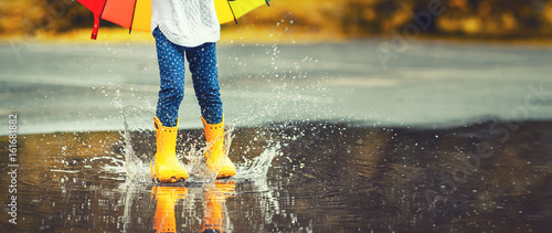 Photo Feet of  child in yellow rubber boots jumping over  puddle in rain