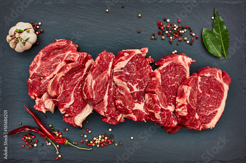 Photography Fresh raw beef steaks with chilly pepper on black slate board