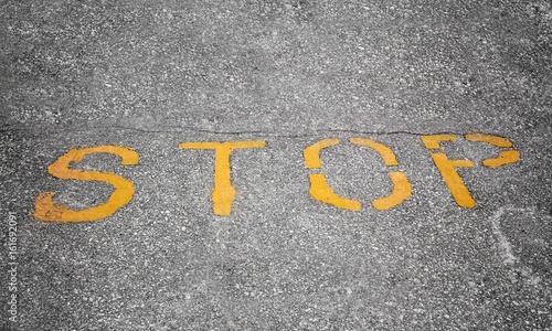 horizontal image of the word"stop" painted in yellow on grey asphalt.