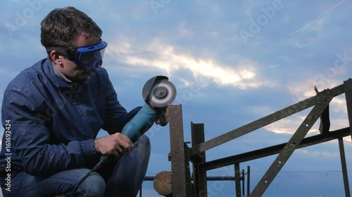 A young man polishes a metal angle grinder at sunset. Beautiful sky behind the worker. photo