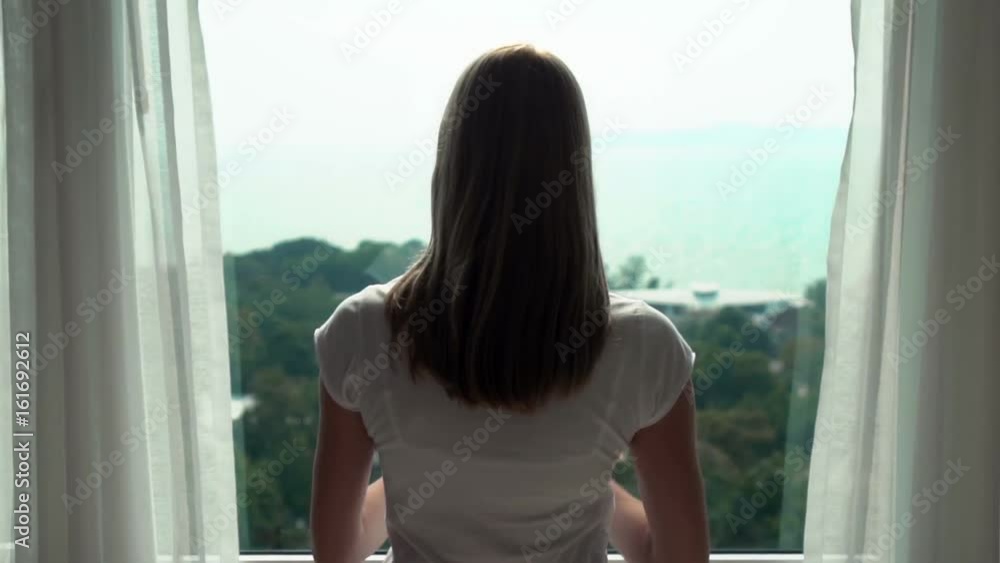 Woman in white t-shirt unveiling curtains and looking out of window. Enjoying the sea view 100 fps Woman in white t-shirt unveiling curtains and looking out of window. Enjoying the sea view 100 fps