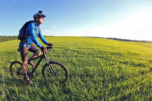 cyclist rides a bicycle on the green field towards the sun © photosaint