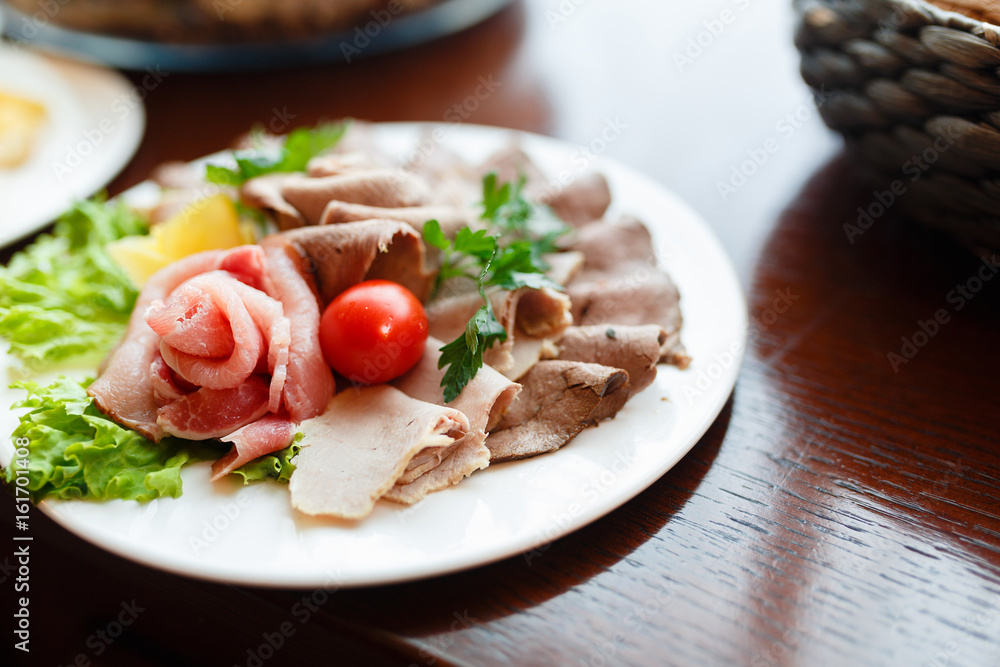 Beautiful patterns, slicing the ham on the plate, snack food. Food plate with delicious salami, pieces of sliced ham, sausage, tomatoes, salad and vegetable - Meat platter with selection