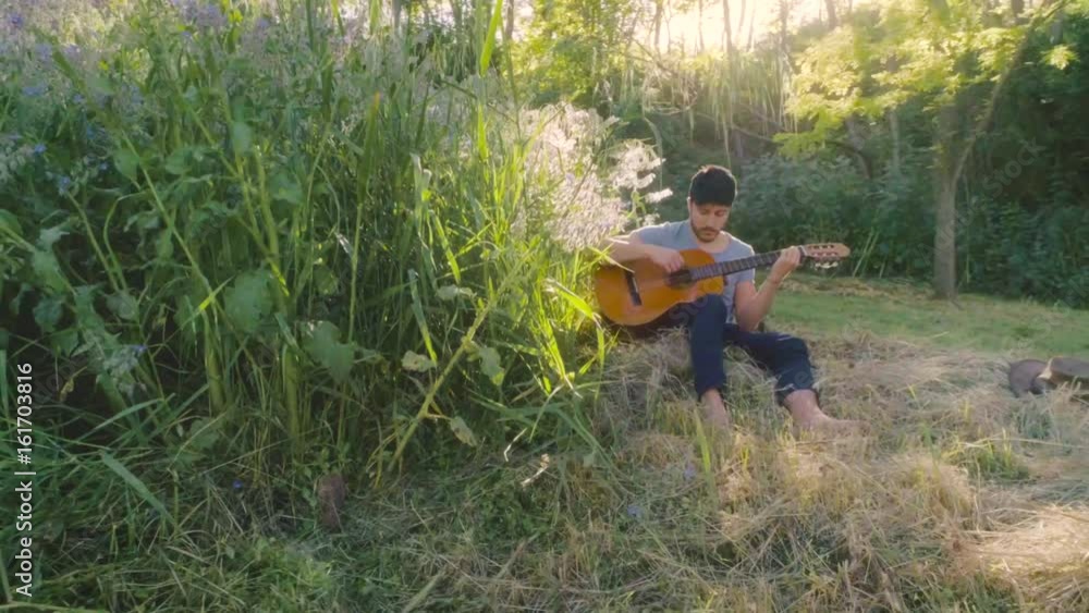 Young man playing guitar under the tree Young man playing guitar under the tree