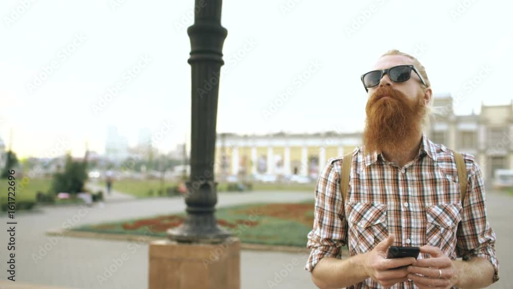 Steadicam shot of Bearded tourist man with backpack walking street and using smartphone for view map outdoors Steadicam shot of Bearded tourist man with backpack walking street and using smartphone for view map outdoors