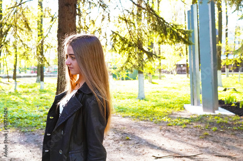 Indifference. A young pretty girl with light brown hair depicts different emotions. The girl is dressed in a black leather jacket and a white dress under her. Sunny spring evening.