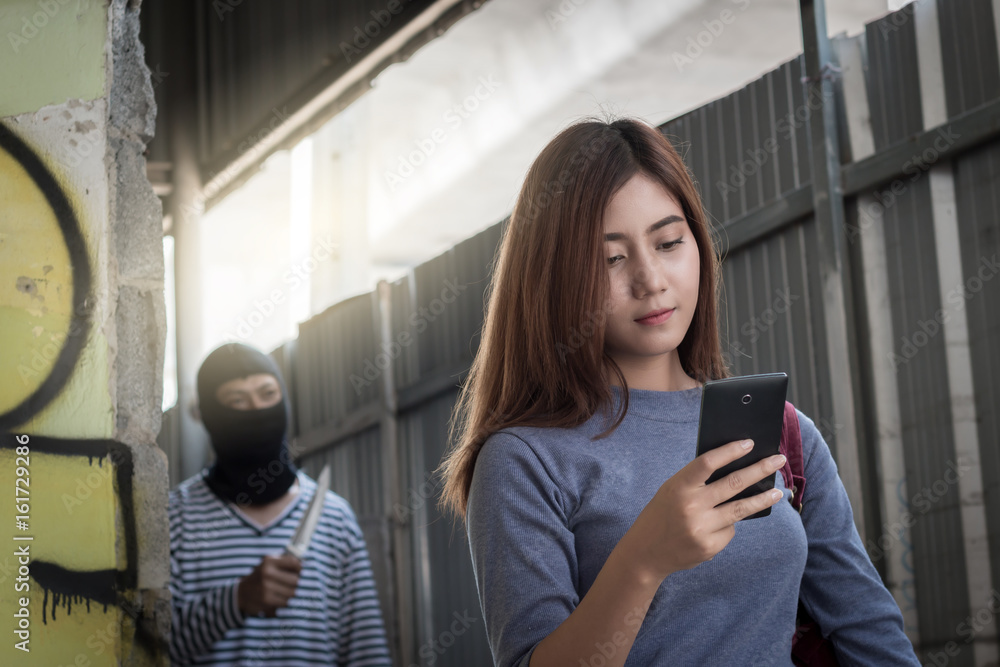 Beautiful young woman holding smartphone and being stalked by man criminal with the knife