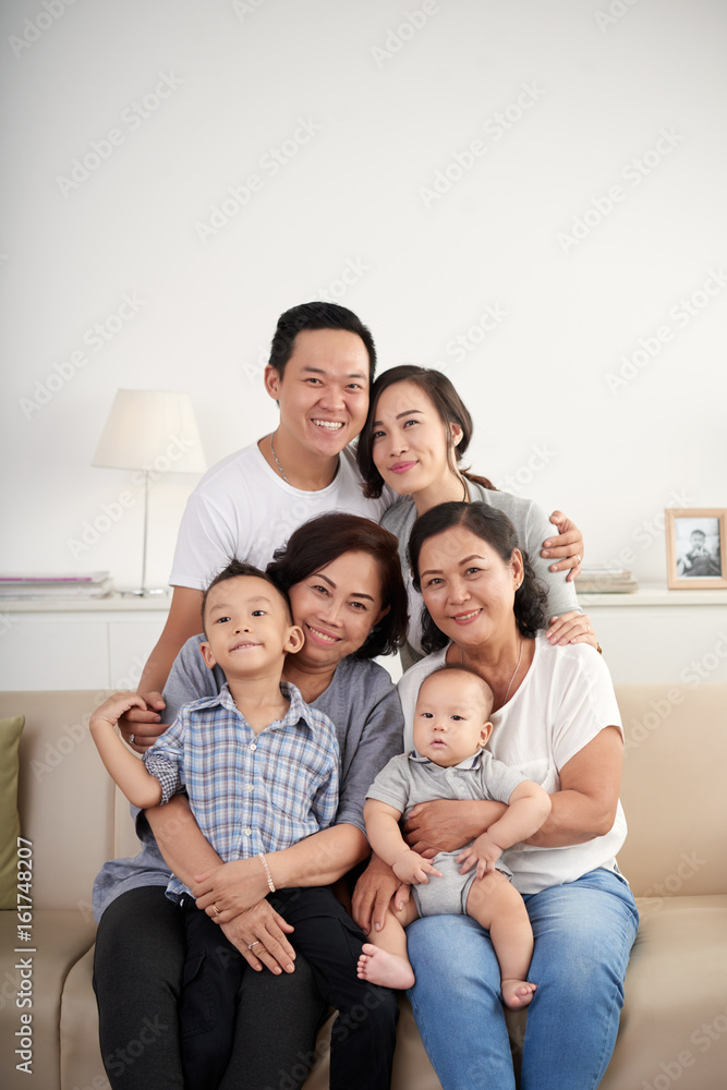 Portrait of big Asian family posing for photo at home sitting on sofa, all smiling happily looking at camera