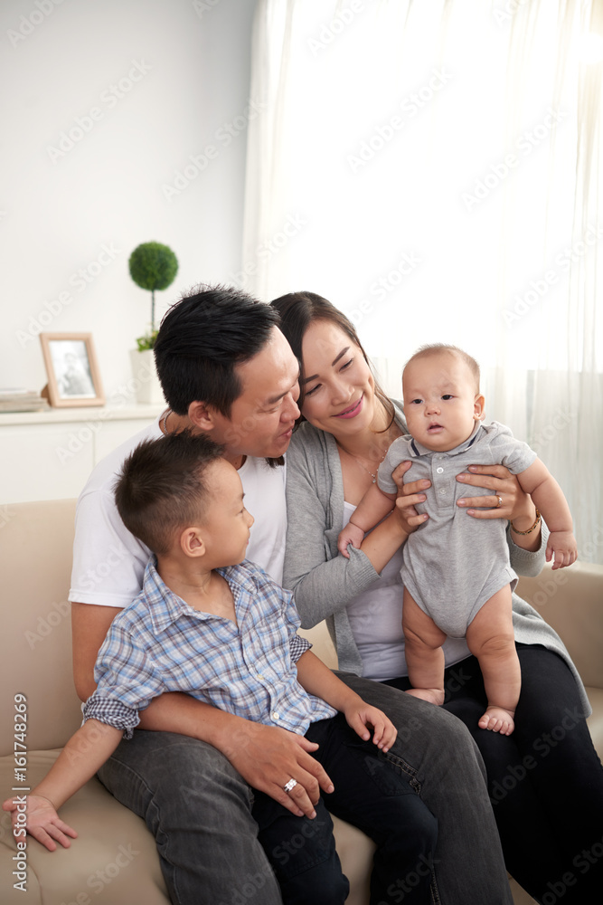 Portrait of young Asian family playing with adorable little kids at home, sitting on sofa Portrait of young Asian family playing with adorable little kids at home, sitting on sofa