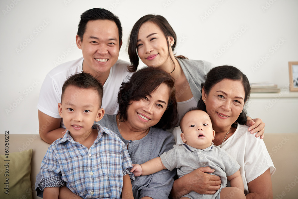 Portrait of big Asian family with two children posing for photo at home, all smiling happily looking at camera Portrait of big Asian family with two children posing for photo at home, all smiling happily looking at camera