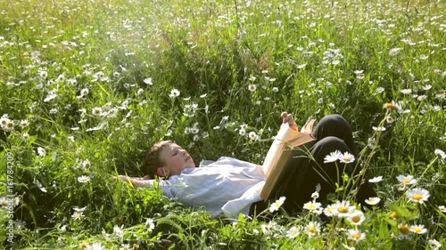 Happy little guy lays in field daisies and reads his favorite book photo