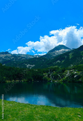 Beautiful mountains lake with a reflection of the high green mountains peaks  on the blue sky background. Amazing Mountain hiking paradise landscape with a lake  no people.