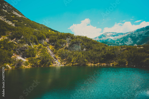 Beautiful mountains lake with a reflection of the high green mountains peaks, on the blue sky background. Amazing Mountain hiking paradise landscape with a lake, no people.