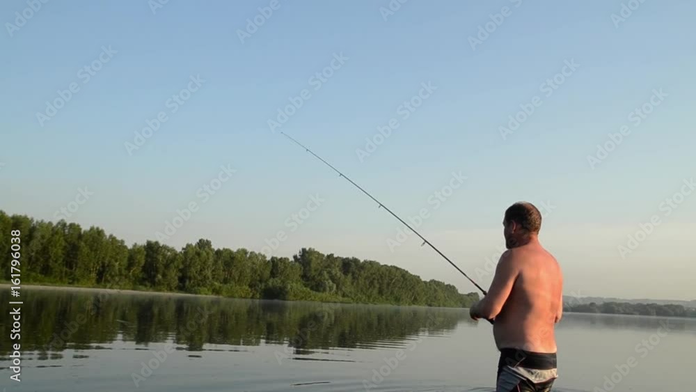 fisherman fishing in a calm river in the morning. Man in fishing gear stending in a river and throws a fishing pole fisherman fishing in a calm river in the morning. Man in fishing gear stending in a river and throws a fishing pole