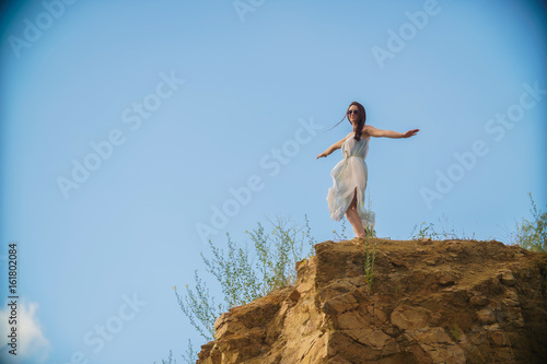 A beautiful romantic girl on the edge of a high cliff dreaming and enjoying a beautiful view
