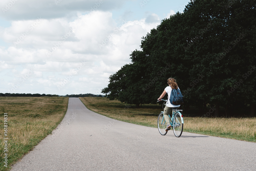 Smiling pretty young woman riding bike in a country road in the park