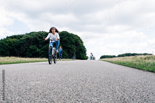 Pretty young woman riding bike in a country road in the park with her family