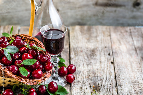 Tableau sur toile Cherry wine in a glass bottle on wooden table