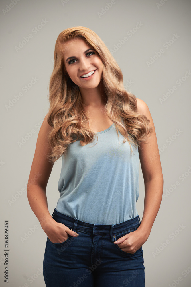 Studio portrait of beautiful blonde woman standing with her hands in pockets and smiling at camera Studio portrait of beautiful blonde woman standing with her hands in pockets and smiling at camera
