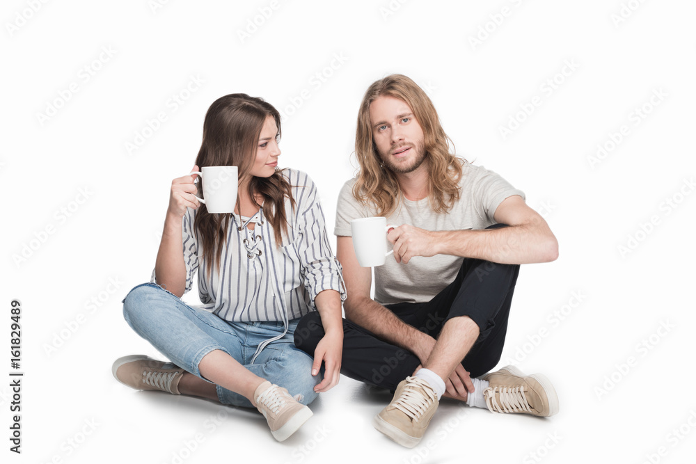 young caucasian couple sitting on floor and drinking coffee, isolated on white young caucasian couple sitting on floor and drinking coffee, isolated on white