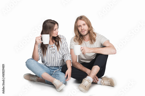 young caucasian couple sitting on floor and drinking coffee, isolated on white