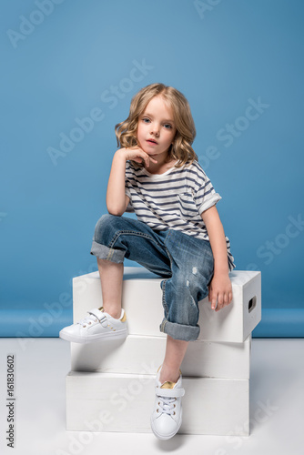 adorable blonde little girl sitting on white boxes and looking at camera