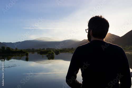 Man looking at beautiful sunrise sunset reflection at Iseo lake in Italy in summer