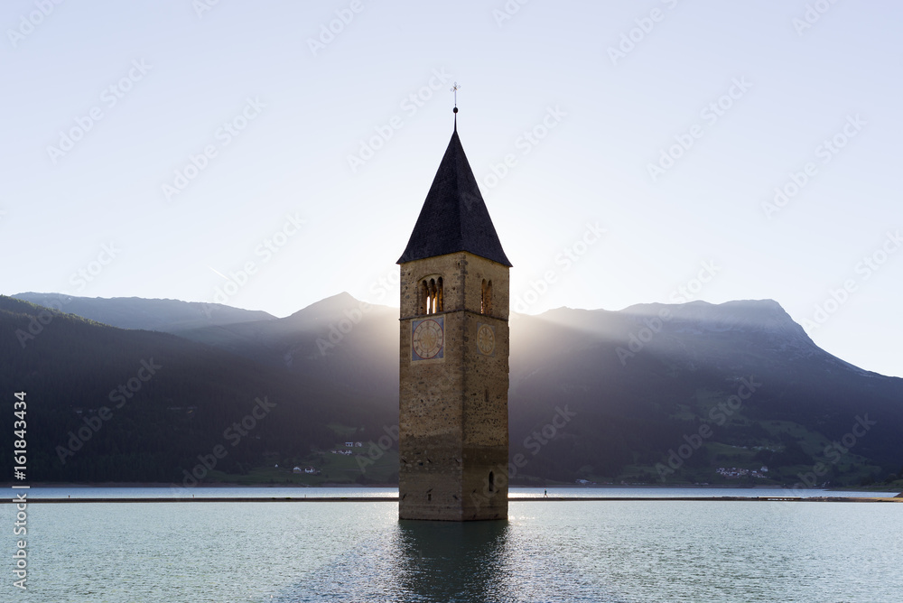 Scenic bell tower with backlit rays of sun submerged in Resia water lake in Alto Adige