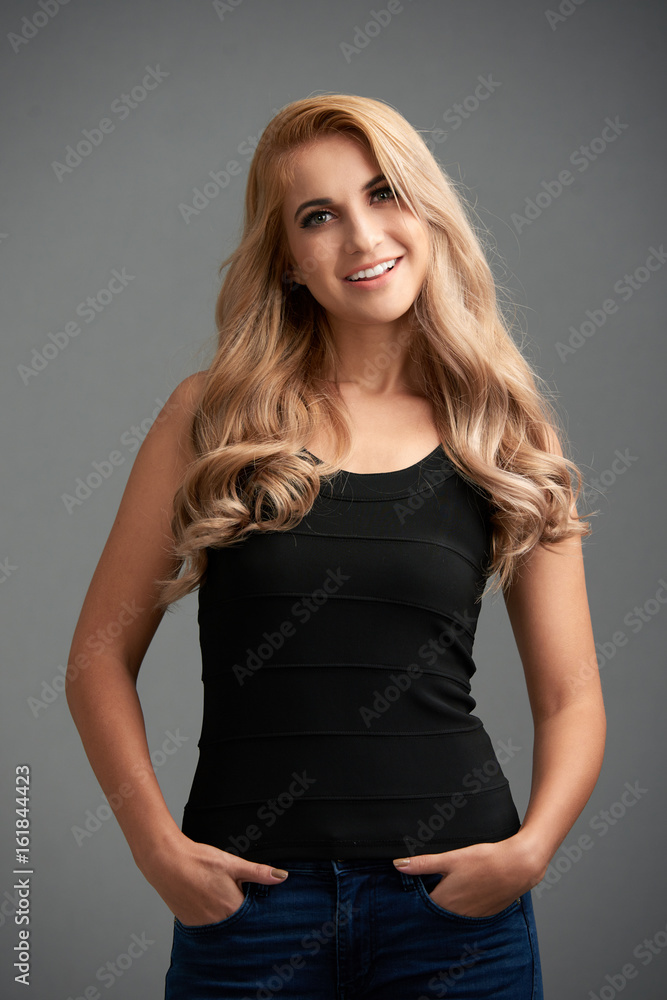 Portrait of charming young woman posing with her hands in pocket against grey background Portrait of charming young woman posing with her hands in pocket against grey background