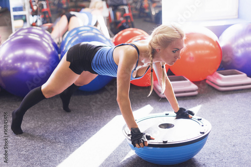 athletic woman doing pushups on a bosu ball in the gym photo