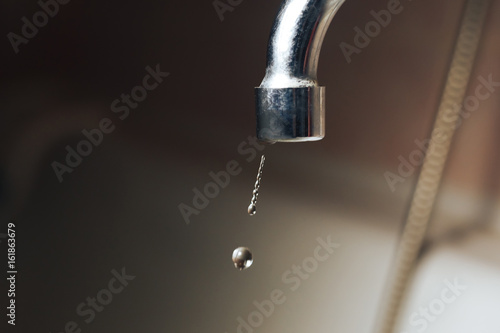 Metal faucet with falling drops of water close-up