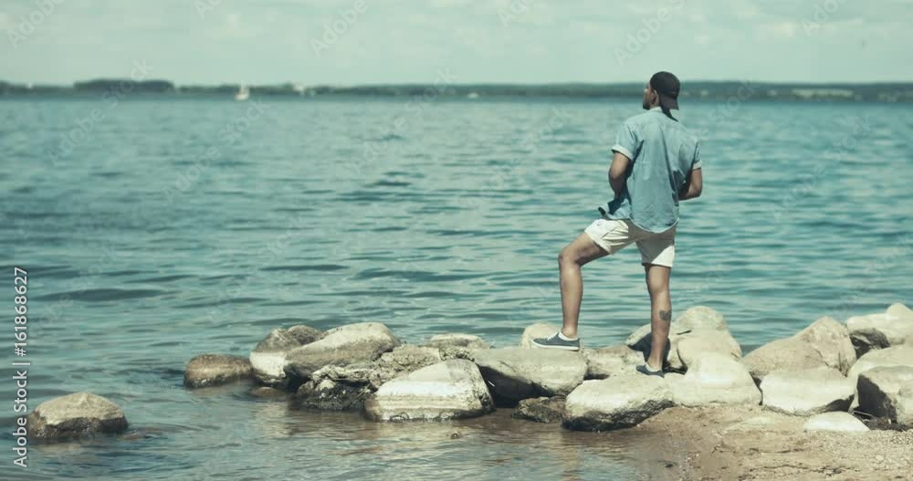 Young adult African American man in casual clothes enjoying summer day, walking on a sea shore Young adult African American man in casual clothes enjoying summer day, walking on a sea shore