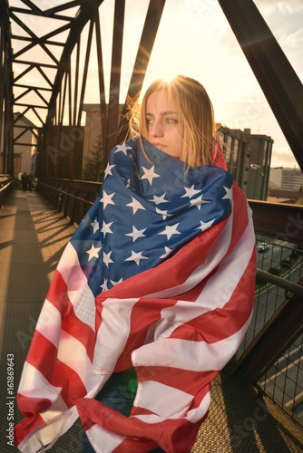 Young woman wrapped in American flag on an iron bridge at dusk of the city photo