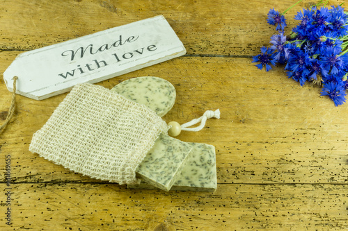 Handmade soap on a rustic wooden board with cornflowers and accessories.