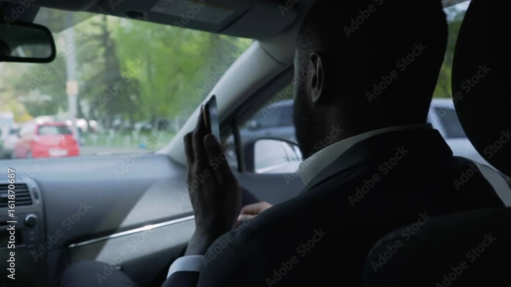 Business man riding in car with personal driver, solving problems by phone Business man riding in car with personal driver, solving problems by phone