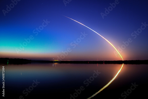 Space Shuttle Launch into a blue sky at dawn with reflection on the water photo