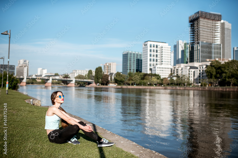 Young woman having resting near the river with great view on the modern Frankfurt city