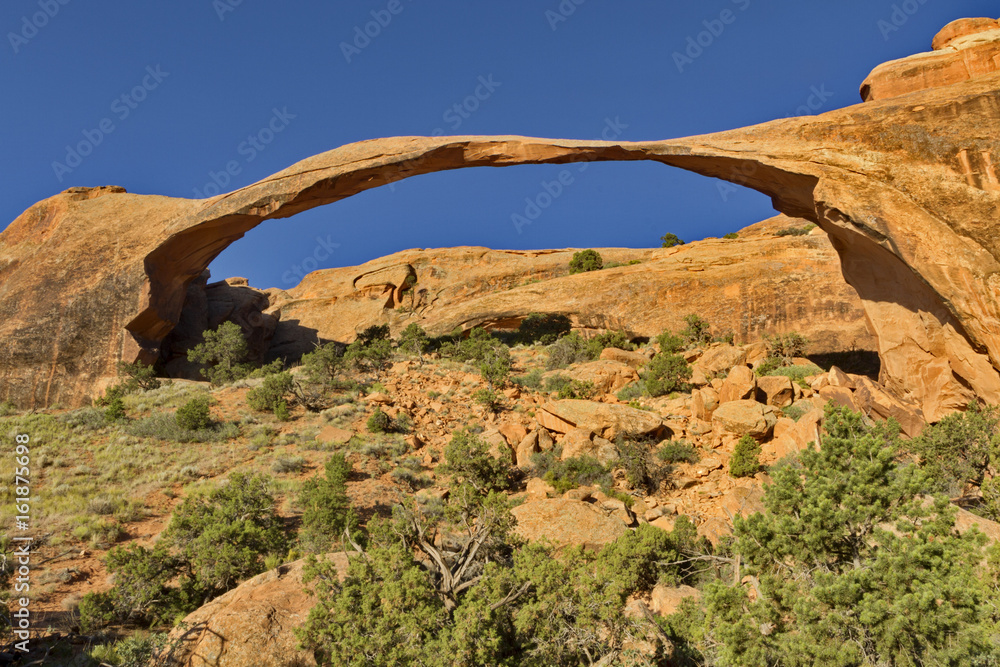Landscape arch with blue sky and view of red desert slope