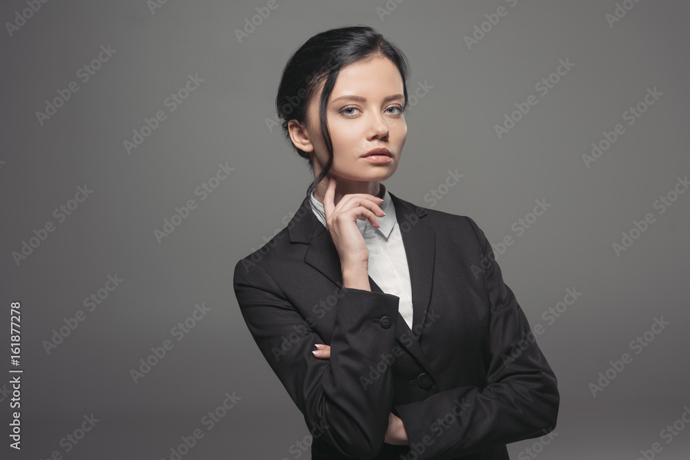 pensive beautiful businesswoman wearing black suit and looking at camera, isolated on grey pensive beautiful businesswoman wearing black suit and looking at camera, isolated on grey