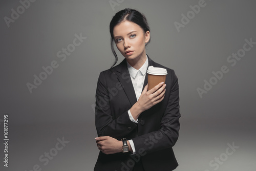 caucasian businesswoman holding paper coffee cup, isolated on grey
