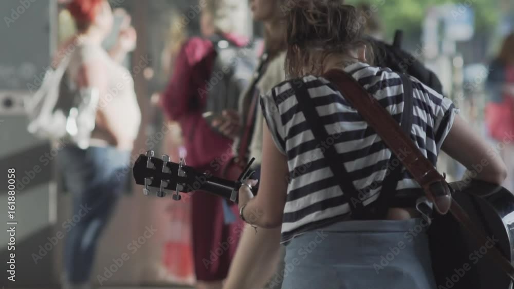 Unidentifiable Young Woman Playing Guitar On A Busy Shopping Street In Berlin In Summer. Slow Motion Shot Unidentifiable Young Woman Playing Guitar On A Busy Shopping Street In Berlin In Summer. Slow Motion Shot