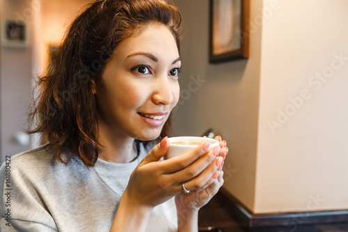 Closeup portrait of happy young indian woman drinking coffee in cafe