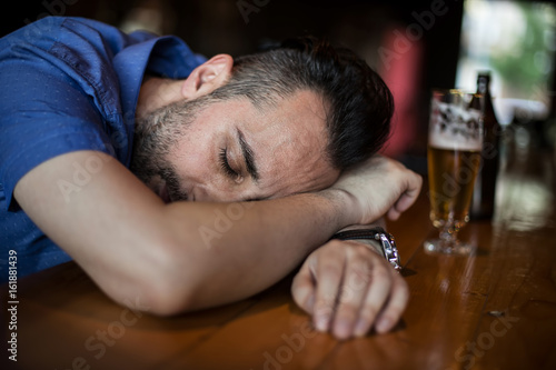 A drunk bearded man holding a glass of beer in his hand and sleeping in the bar
 photo