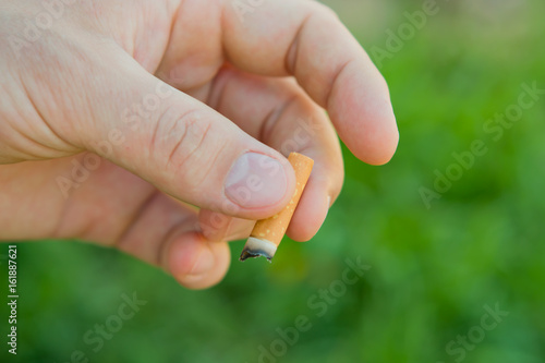 Cigarette in the man's hand on a background of green grass blur. The concept of a healthy lifestyle, the dangers of Smoking