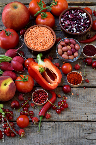 composition of red vegetarian products: fruits, vegetables, spices and beans on wooden background. Apple tomatoes, currant peppers, raspberries cherry, lentils. Healthy food. Copy space for text