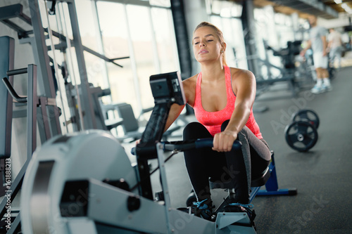 Young cute woman doing exercises with rowing machine