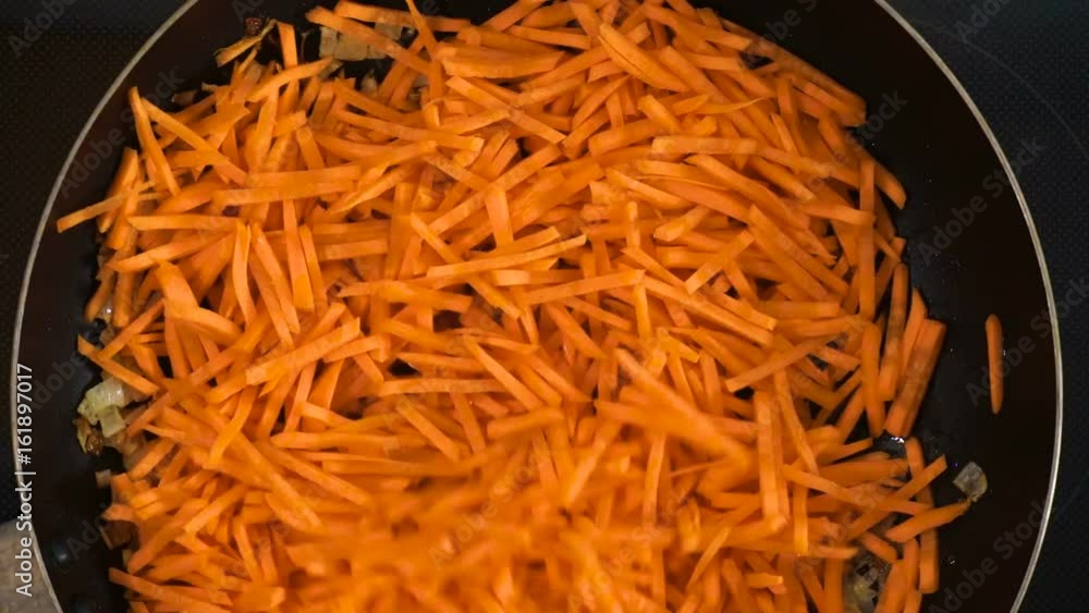 Finely chopped onion and carrot are fried in a hot frying pan. A cook with a wooden spatula stirs the food. Fried onion, carrot as an ingredient for cooking. Finely chopped onion and carrot are fried in a hot frying pan. A cook with a wooden spatula stirs the food. Fried onion, carrot as an ingredient for cooking.