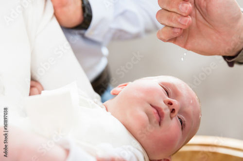 Baby weint bei der Taufe als der Pfarrer Weihwasser auf seinen Kopf träufelt