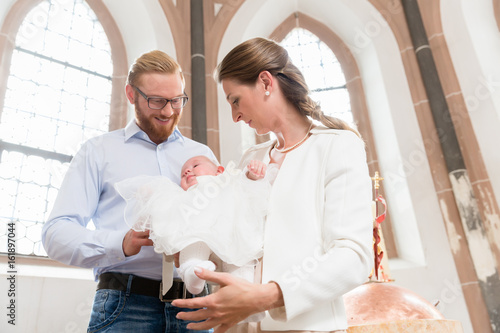 Junge Eltern mit ihrem Baby im Taufkleid in einer Kirche photo